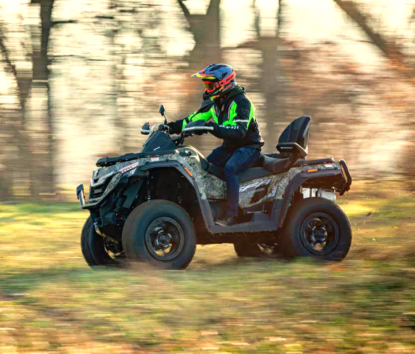 Person auf einem QJ Motor SFA 1000 Touring Quad in Camouflage-Farbgebung fährt durch ein bewaldetes Gelände